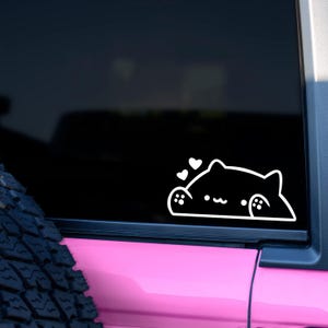 Puede incluir: Una pegatina de vinilo blanco de un gato negro con corazones encima, en un coche rosa.