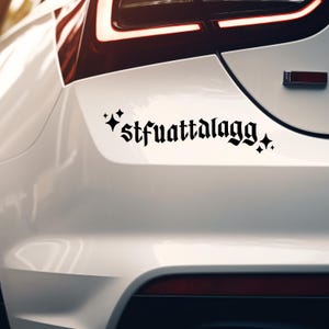 May include: Black vinyl car decal featuring the text "stfuattalagg" in a gothic font, with starburst accents. The sticker is applied to the white rear of a vehicle.