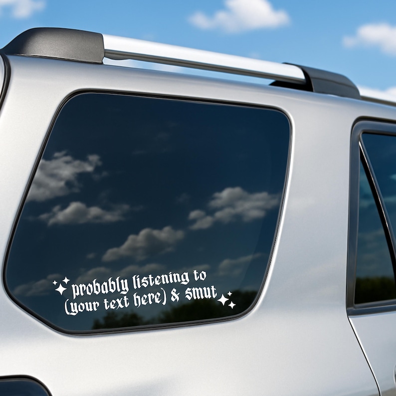 May include: White vinyl decal for a car window. The text reads "probably listening to (your text here) & smut" in a gothic font, with starburst accents. The decal is on a silver vehicle with a blue sky background.
