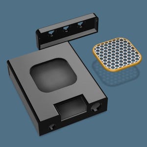 May include: A black rectangular device with a square cutout, a smaller rectangular opening, and two circular holes. A separate black rectangular piece with three holes and a yellow and white honeycomb-patterned square are also present.