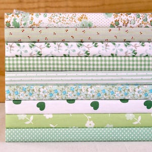May include: A collection of fabric rolls in green and white. The patterns include floral, polka dots, stripes, and gingham. The fabrics are tightly rolled and stacked, displaying a variety of designs suitable for sewing or craft projects.