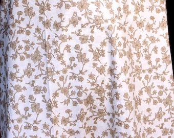 May include: White fabric with a repeating pattern of tan floral designs. The flowers and leaves are detailed and create a delicate, vintage aesthetic. The fabric appears to be a light material, possibly cotton or linen.