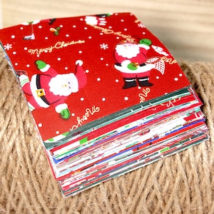 Puede incluir: Una pila de cuadrados de tela con temática navideña. El cuadrado superior presenta un fondo rojo con lunares blancos e ilustraciones de Papá Noel. Las palabras "Merry Christmas" están escritas en escritura blanca. Los bordes de la tela son visibles.
