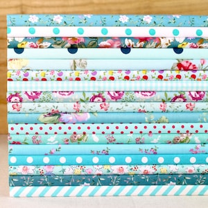 May include: A stack of various patterned fabric rolls in shades of blue, teal, and white. The patterns include floral, polka dots, gingham, and stripes. The fabrics are neatly stacked, showcasing a variety of designs suitable for sewing and crafting projects.