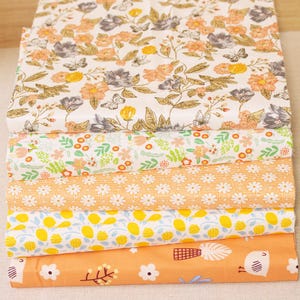 May include: Five different fabric swatches with floral and geometric patterns. The top swatch features a white background with brown, orange, and gray floral designs. The second swatch has a white background with green leaves and small pink flowers. The third swatch has a white background with small orange flowers. The fourth swatch has a white background with yellow lemons and blue leaves. The bottom swatch has an orange background with small white flowers and a bird illustration.