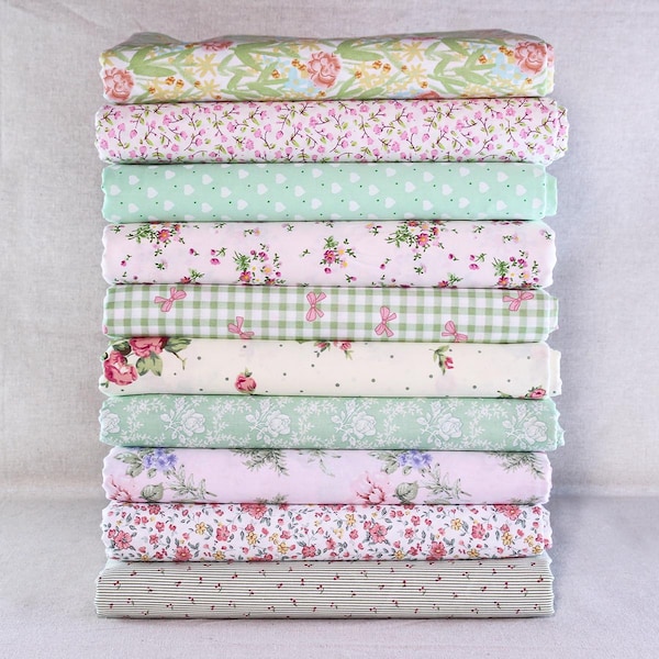May include: A stack of ten folded fabric pieces with floral, polka dot, and gingham patterns. The fabrics feature a variety of colors, including pink, green, and white. The patterns include roses, hearts, and bows. The fabrics are likely cotton or a similar material.