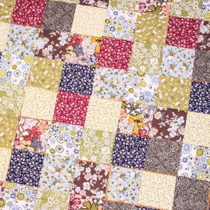 Pode incluir: Close-up de um edred&atilde;o de patchwork com uma variedade de tecidos florais e estampados. O edred&atilde;o apresenta quadrados em tons de vermelho, amarelo, verde, azul e castanho. O design &eacute; uma mistura de pequenas estampas florais e cores lisas.