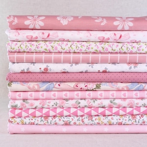 Può includere: Una pila di tessuti rosa con vari motivi, tra cui floreali, pois, fiocchi e forme geometriche. I tessuti sono in tonalità rosa chiaro e medio, creando una collezione coesa e visivamente accattivante. Ideale per progetti di cucito e artigianato.
