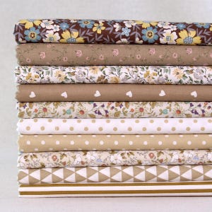 May include: A stack of fabric bolts in various floral and geometric patterns. The fabrics feature a range of colors, including brown, beige, white, and yellow. Some fabrics have polka dots, hearts, and floral designs.