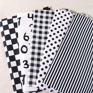 Op de afbeelding: Vijf verschillende zwart-witte stofstalen. De stalen hebben een geruit patroon, een gingham-patroon, stippen, strepen en een witte stof met zwarte cijfers erop.