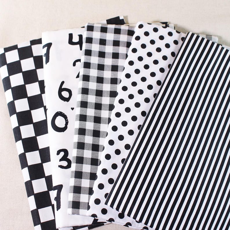 Op de afbeelding: Vijf verschillende zwart-witte stofstalen. De stalen hebben een geruit patroon, een gingham-patroon, stippen, strepen en een witte stof met zwarte cijfers erop.
