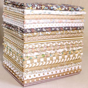 May include: A stack of 25 fabric squares in various brown and white patterns, including floral, geometric, and polka dot designs. The fabric squares are arranged in a neat pile, showcasing the different patterns and colours.