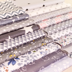 Può includere: Un mucchio di ritagli di tessuto in vari motivi e colori, tra cui grigio, bianco e rosa. I tessuti presentano disegni geometrici, motivi floreali e stampe animalier.