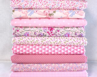 May include: A stack of ten rolled fabric pieces in various shades of pink. The fabrics feature floral, star, polka dot, and geometric patterns. The fabrics are suitable for quilting, sewing, and crafting projects.