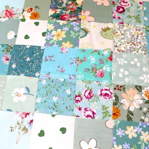 Puede incluir: Una colcha de retazos con una variedad de patrones florales en tonos de azul, verde y blanco. La colcha está hecha de cuadrados de diferentes telas, cada uno con un diseño único.