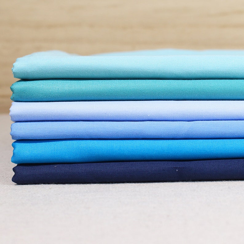 May include: Stack of six fabric swatches in shades of blue, from light blue to dark blue.