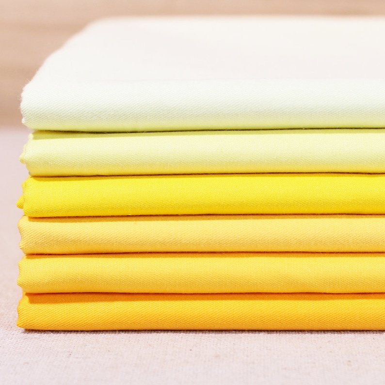 May include: A stack of fabric swatches in shades of yellow and green. The fabric is a smooth, woven cotton with a subtle texture.