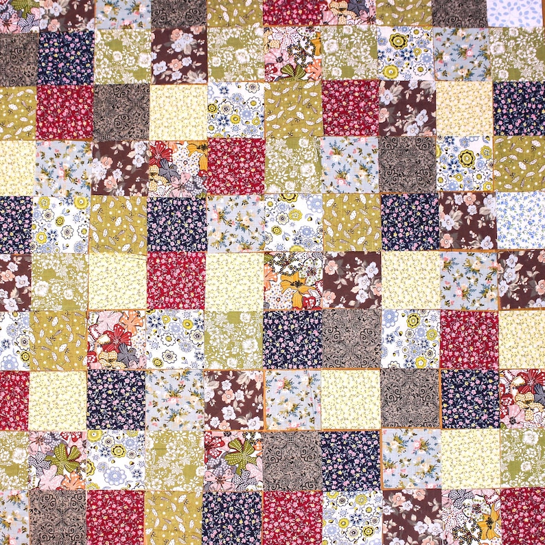 Pode incluir: Um edredom de retalhos com um padr&atilde;o repetitivo de quadrados em v&aacute;rios tecidos florais e estampados. Os quadrados apresentam cores como vermelho, azul, verde e castanho, criando um design visualmente atraente e texturizado.