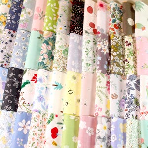 Könnte beinhalten: Eine Sammlung gerollter Stoffballen mit verschiedenen floralen Mustern. Die Stoffe zeigen Designs mit Blumen und Blättern in Blau-, Rosa-, Grün- und Gelbtönen. Die Kollektion umfasst eine Vielzahl von Mustern.