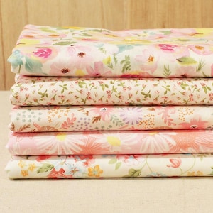 Pode incluir: Uma pilha de seis peças de tecido dobradas com estampas florais. Os tecidos apresentam vários desenhos com flores rosa, amarelas e verdes sobre um fundo branco. Os tecidos são empilhados ordenadamente, mostrando as diferentes estampas florais.