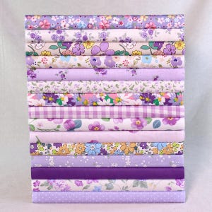 Pode incluir: Uma pilha de quinze rolos de tecido dobrados com vários padrões em tons de roxo, lavanda e lilás, incluindo estampas florais, xadrez vichy e bolinhas. A coleção exibe uma gama de tons desde o pastel claro até o violeta profundo.