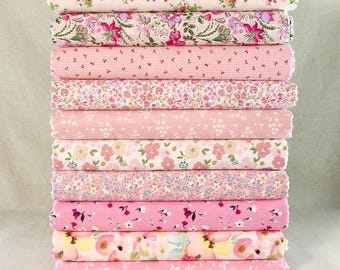 May include: A pile of ten rolls of pink fabric, each with a different floral or patterned design. The fabrics feature small and large floral prints, stripes, and polka dots. The color scheme is predominantly pink, with touches of white, green, and yellow.