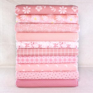 Peut inclure: Une pile de tissus roses avec divers motifs, dont des fleurs, des pois, du vichy et des motifs célestes. Les tissus sont dans des tons de rose clair et moyen, créant une collection cohérente et visuellement attrayante. Les tissus sont pliés et empilés avec soin.
