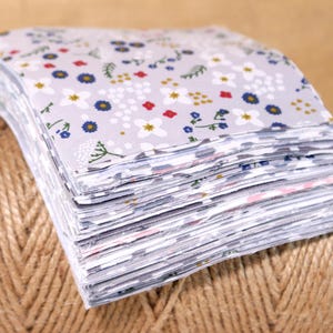 May include: A stack of gray fabric squares with a white floral pattern. The fabric has small white flowers, red flowers, blue flowers, and green leaves.