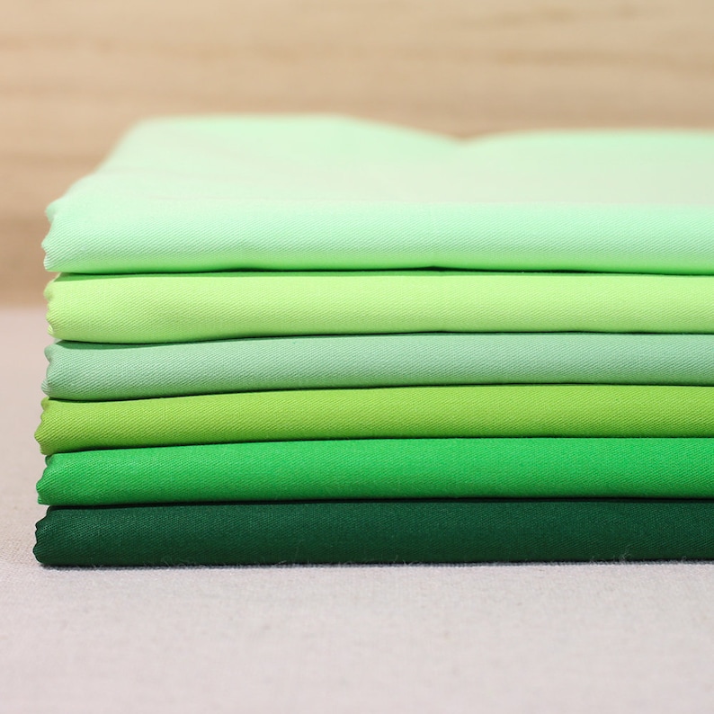 May include: A stack of eight fabric swatches in shades of green, ranging from light green to dark green.