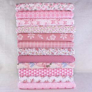 Peut inclure: Une pile de rouleaux de tissu rose avec divers motifs, notamment floraux, vichy, nœuds et géométriques. Les tissus, dans des tons de rose et de blanc, sont parfaits pour la couture et les travaux manuels.