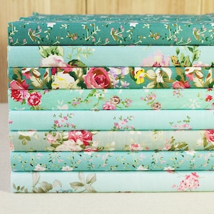 May include: A stack of ten fabric squares with floral patterns in shades of green and blue. The fabric is soft and has a delicate feel.