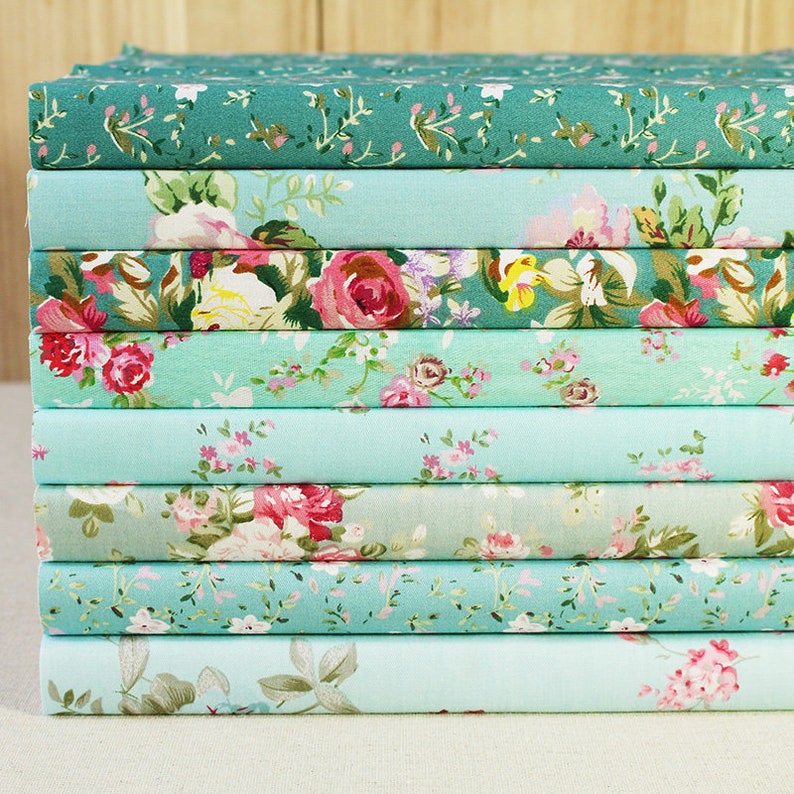May include: A stack of ten fabric squares with floral patterns in shades of green and blue. The fabric is soft and has a delicate feel.