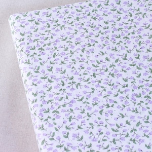 Puede incluir: Tela blanca con un peque&ntilde;o estampado floral morado. Las flores est&aacute;n dispuestas en un patr&oacute;n repetitivo en la tela.