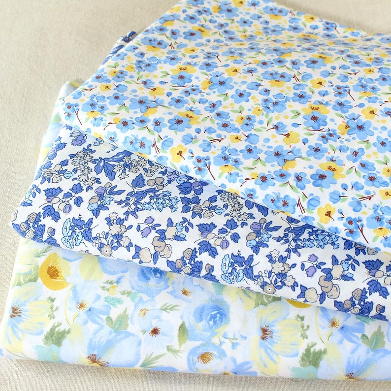 Puede incluir: Tres capas de tela floral en tonos azules, amarillos y blancos. La capa superior presenta peque&ntilde;as flores azules y amarillas sobre un fondo blanco. La capa intermedia tiene un patr&oacute;n de flores azules y moradas. La capa inferior tiene grandes flores azules y amarillas.