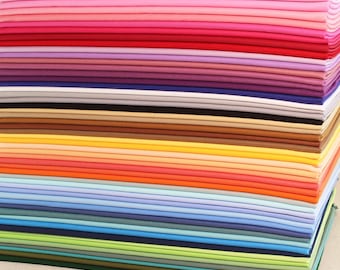 May include: A stack of folded fabric in a spectrum of colors, ranging from light pink to deep green. The layers of fabric are neatly arranged, showcasing a variety of hues including red, orange, yellow, blue, and purple. The image highlights the texture and color variations.