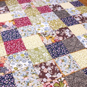 Pode incluir: Um edredom de retalhos composto por in&uacute;meros quadrados de tecido com v&aacute;rios padr&otilde;es florais e cores. O edredom apresenta quadrados em tons de vermelho, azul, verde, amarelo e castanho, criando um design vibrante e texturizado. &Eacute; um artigo feito &agrave; m&atilde;o.
