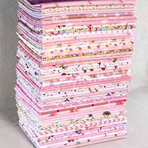 May include: A large pile of folded pink fabrics, showcasing a range of patterns including florals, polka dots, and stripes. The fabrics vary in texture and design, suitable for sewing and craft projects. The stack is a mix of light and dark pinks.