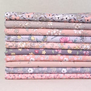 Könnte beinhalten: Ein Stapel Stoffe mit Blumenmustern in verschiedenen Pastellfarben. Die Stoffe weisen zarte Blumenmuster in Rosa, Grau und Weiß auf. Der Stoff scheint aus Baumwolle oder einem ähnlichen Material zu bestehen, das sich für Quilt- oder Bastelprojekte eignet.