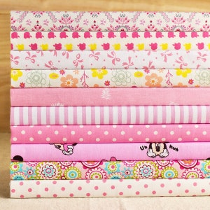 May include: A stack of pink and white fabric scraps with various patterns, including polka dots, stripes, flowers, and a Mickey Mouse design. The fabric scraps are arranged in a neat pile.
