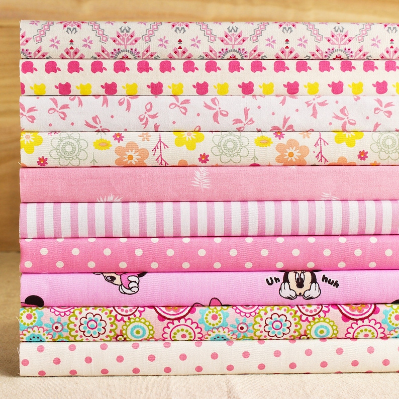 May include: A stack of pink and white fabric scraps with various patterns, including polka dots, stripes, flowers, and a Mickey Mouse design. The fabric scraps are arranged in a neat pile.