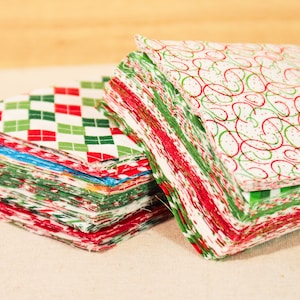 May include: Two stacks of fabric squares in red, green and white patterns. The fabric squares are stacked on top of each other and are ready to be used for quilting or other crafts.