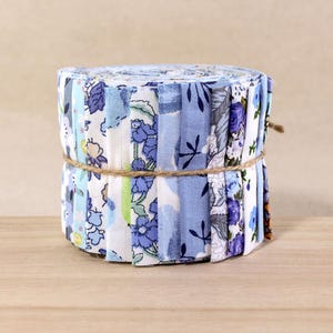 Puede incluir: Un rollo de tiras de tela en tonos azules, blancos y morados, con estampados florales. La tela está atada con hilo. El rollo está sobre una superficie de madera.