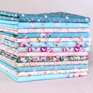 May include: A stack of folded fabric in various floral patterns. The fabrics feature a range of colors, including blue, pink, and green, with designs of roses and other flowers. The fabrics are stacked neatly, showcasing the variety of patterns.