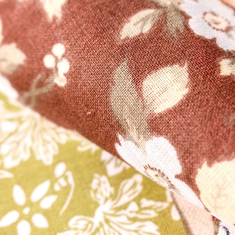Pode incluir: Close-up de tecido floral em tons de castanho, creme e verde. O tecido tem uma apar&ecirc;ncia texturizada com um padr&atilde;o repetido de flores e folhas. A imagem destaca os detalhes do t&ecirc;xtil.