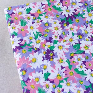 Puede incluir: Una tela blanca con un estampado floral con flores rosas, moradas y verdes. Las flores son de dise&ntilde;o de margarita con centros amarillos.