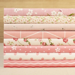 May include: A stack of eight pink fabric-covered notebooks with different patterns, including floral, geometric, and polka dots.