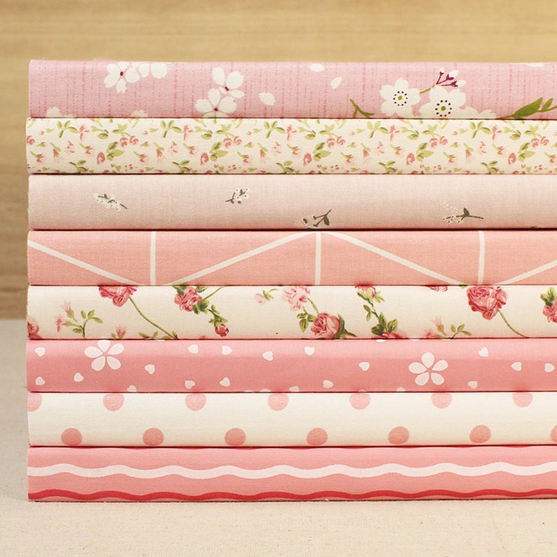 May include: A stack of eight pink fabric-covered notebooks with different patterns, including floral, geometric, and polka dots.