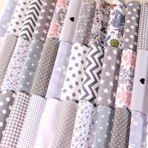 Könnte beinhalten: Eine Sammlung von 20 Stoffquadraten in verschiedenen Grautönen und Weiß mit unterschiedlichen Mustern, darunter Punkte, Sterne und Blumenmuster.