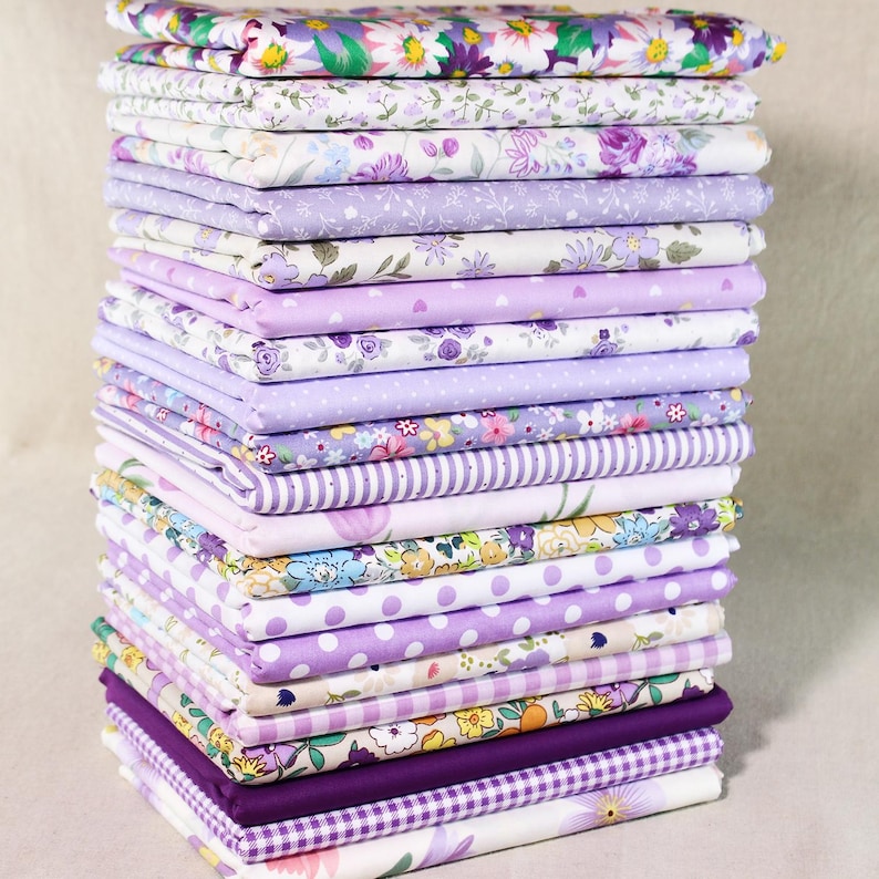 Puede incluir: Una pila de 20 cuadrados de tela p&uacute;rpura y blanca con varios patrones florales, de lunares y rayas. La tela es perfecta para acolchar, manualidades y proyectos de costura.