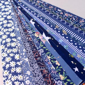 May include: A collection of long, narrow strips of paper arranged in a fan shape, featuring various patterns in shades of navy blue, light blue, and white, including daisies, stars, gingham checks, paisley, and floral botanical designs.